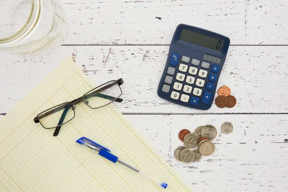 Calculator, coins, glasses and a ledger sheet on a desk for GST e-invoicing calculations