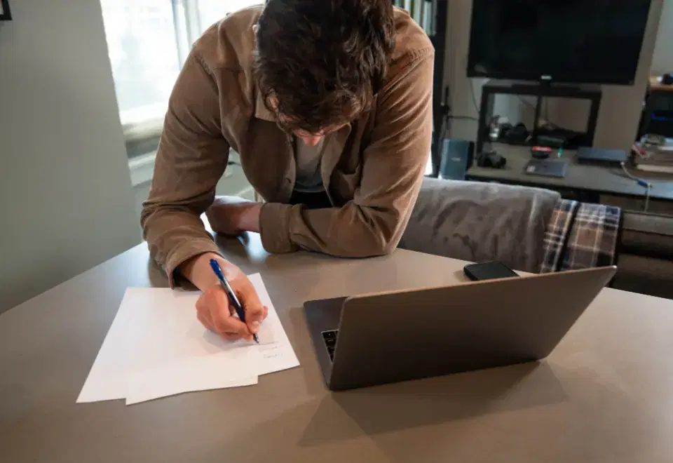 Remote developer writing notes beside a laptop while working from a home office