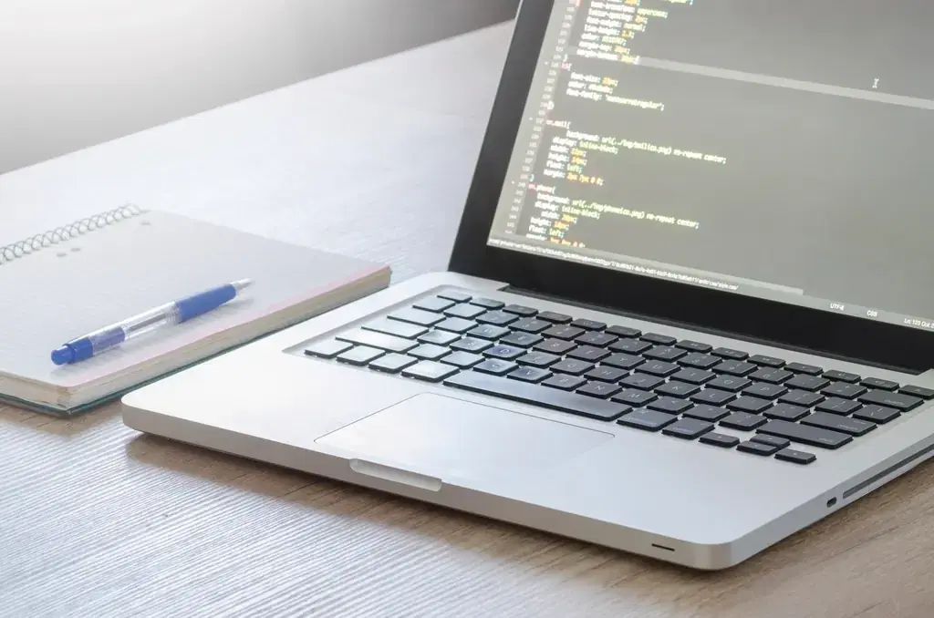Laptop showing CSS code for a WordPress website on a desk beside a notebook