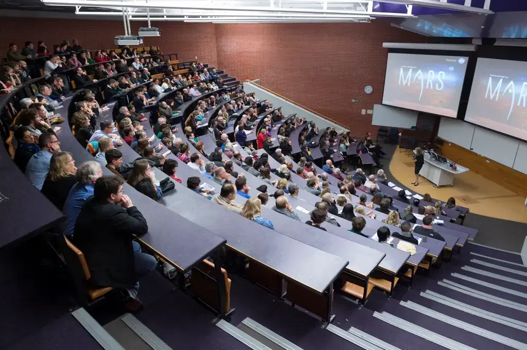 Students attending a lecture in a tiered university lecture hall with projection screens