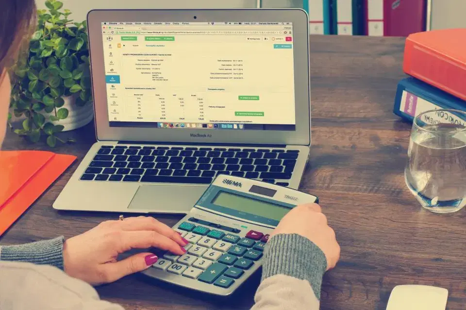 Accountant using a calculator next to a laptop showing accounting software on an office desk