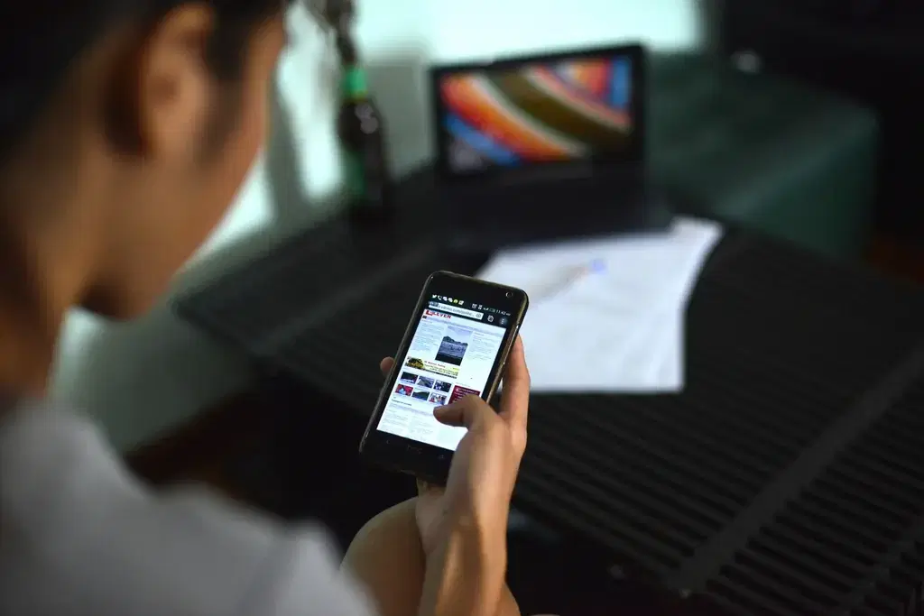Person reading a fintech app on a smartphone with a laptop in the background