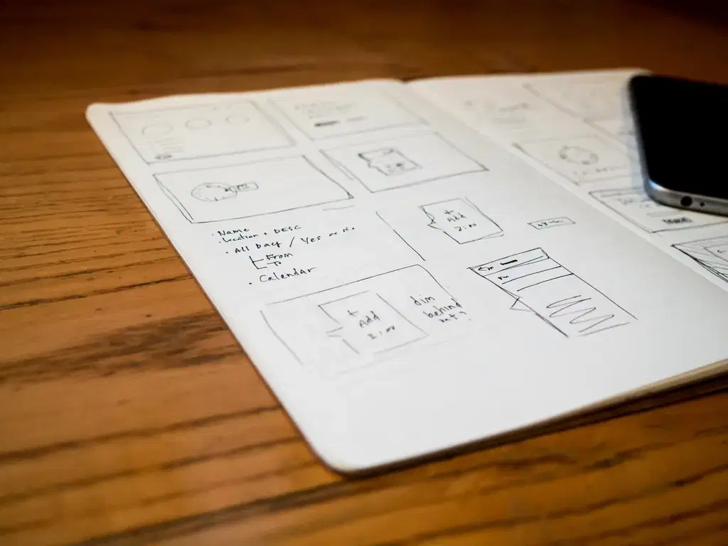 Hand-drawn mobile app wireframe sketches in a notebook next to a smartphone
