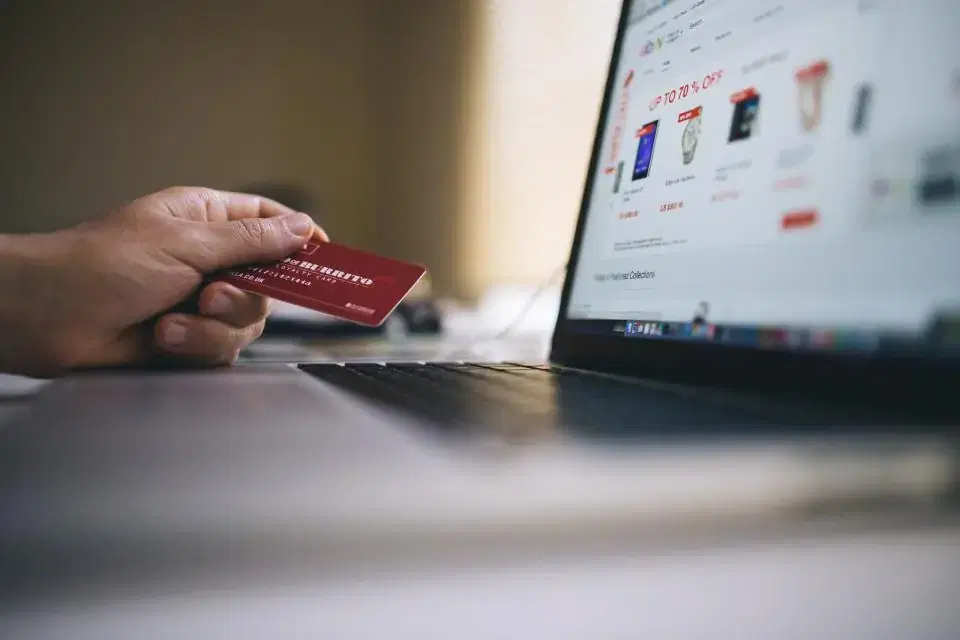 Shopper holding a credit card in front of a laptop for an online payment gateway checkout