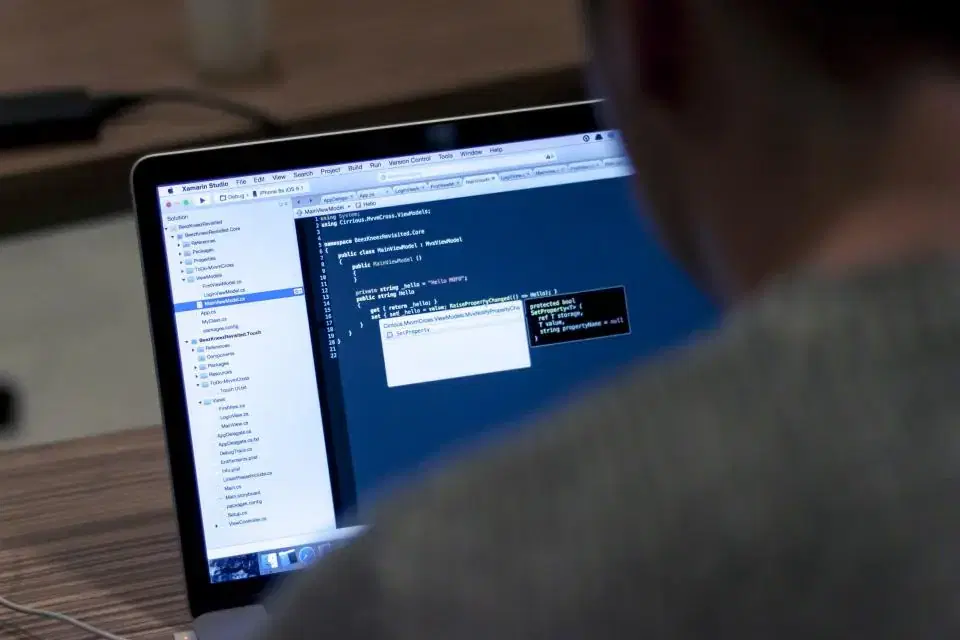 Full-stack developer writing code on a laptop, seen over the shoulder