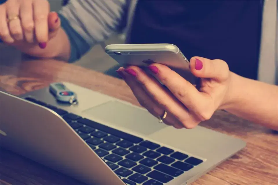 Woman holding a smartphone above a laptop keyboard while chatting with an AI chatbot