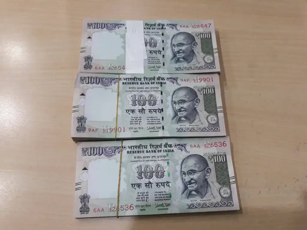 Bundles of Indian hundred-rupee notes on a table, representing chit fund collections