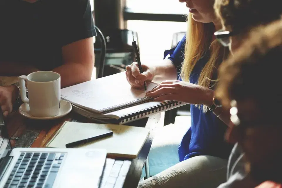 Sales team taking notes around a table with laptops and coffee during a CRM planning meeting