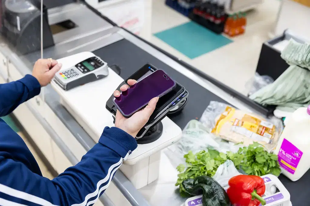 Shopper paying with a smartphone at a card terminal at a supermarket checkout counter