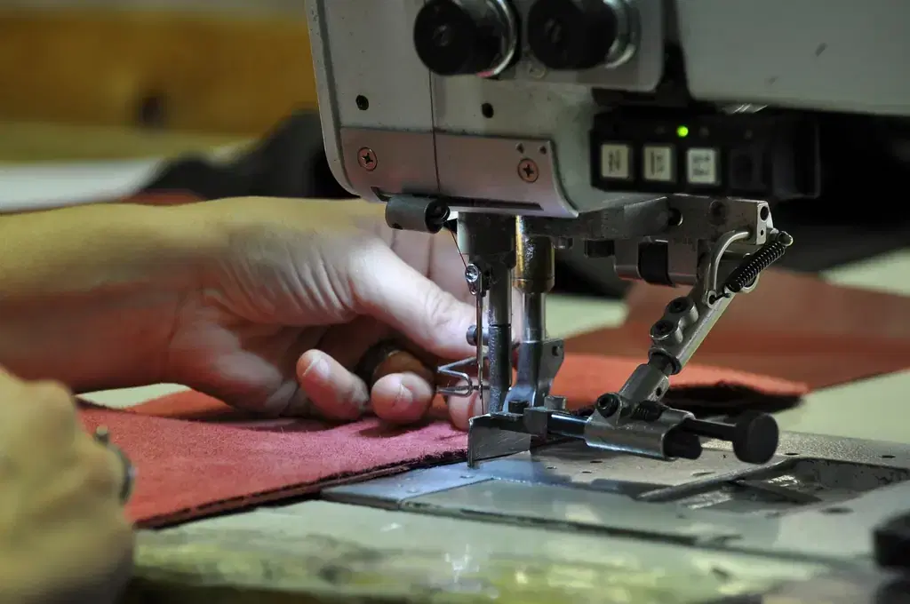 Hands guiding fabric under an industrial sewing machine in a garment factory
