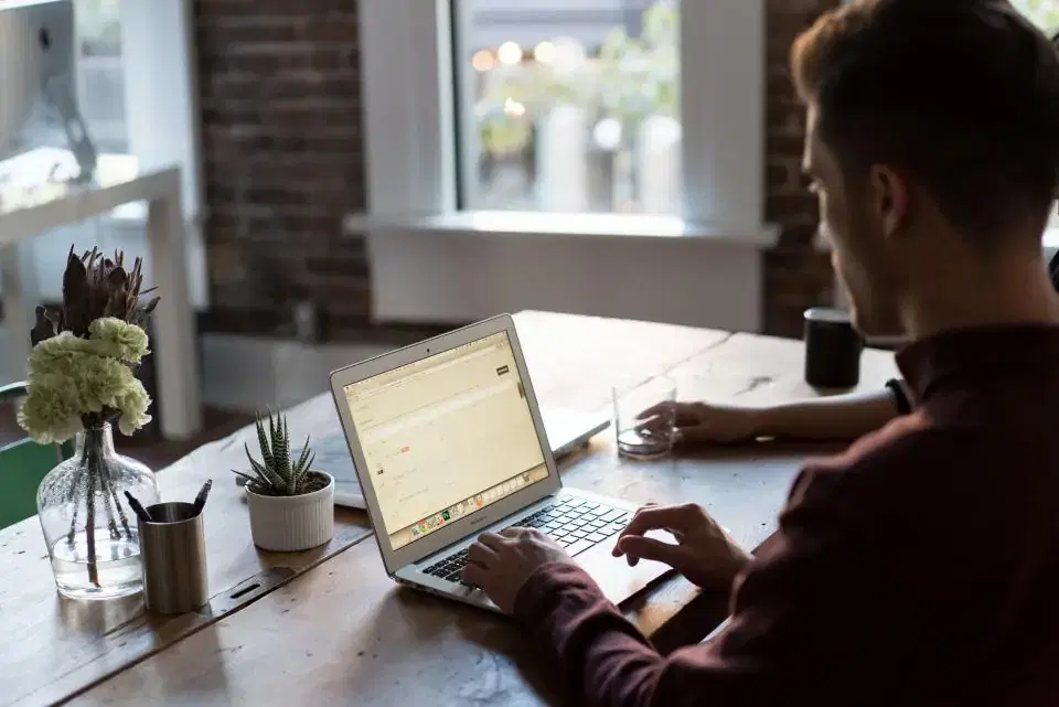 Web developer typing on a laptop at a wooden desk while maintaining a website